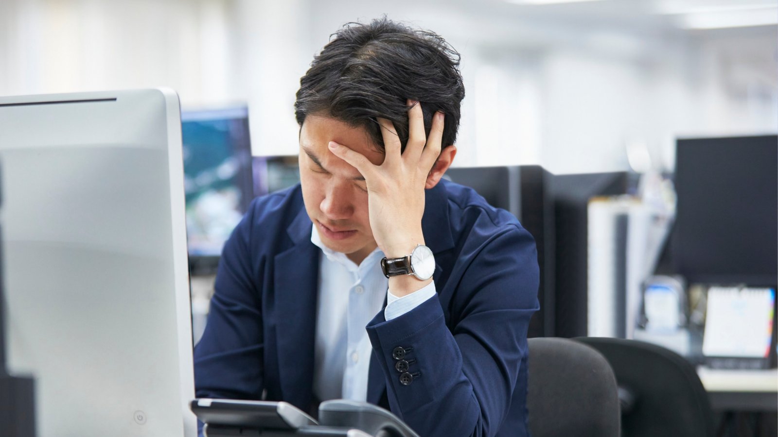 A stressed office worker at a desk with a hand on their forehead.